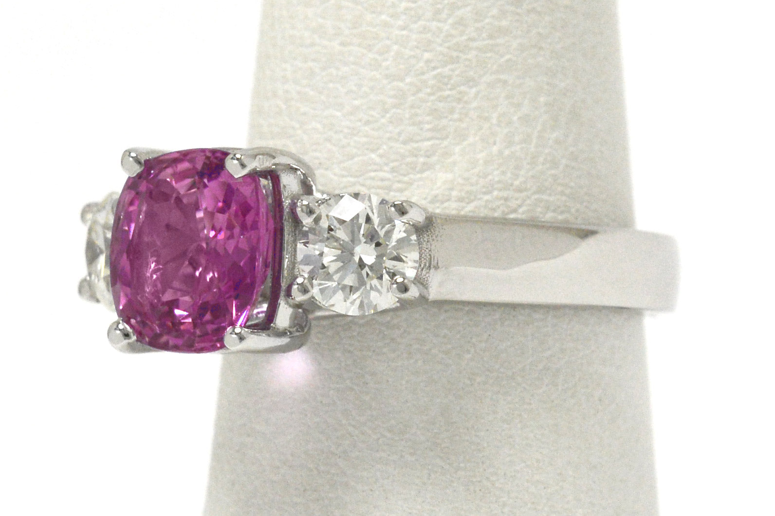 The antique cushion pink sapphire is accented by 2 white diamonds.