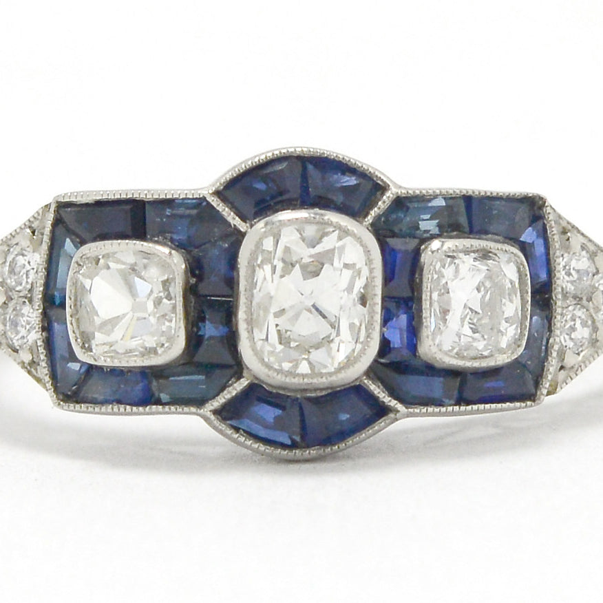 A 3 old mine cushion cut diamond engagement ring accented surrounded by blue sapphires.