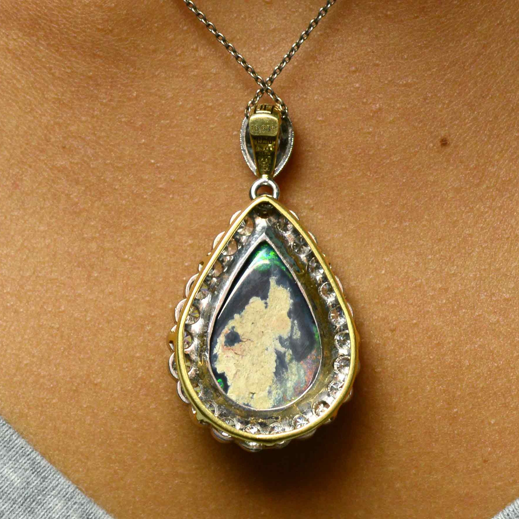 A teardrop shaped black opal platinum pendant with a halo of diamonds.