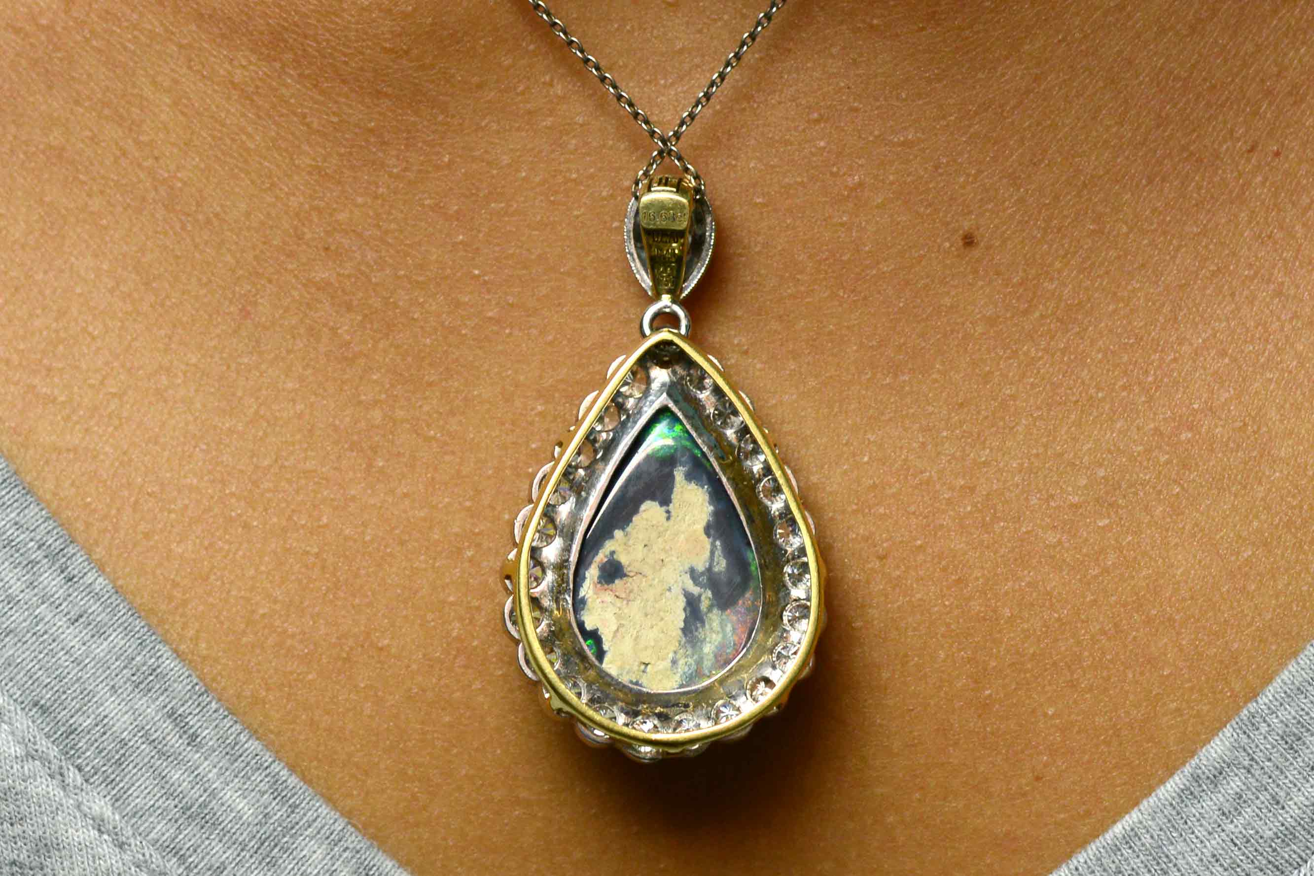 A teardrop shaped black opal platinum pendant with a halo of diamonds.