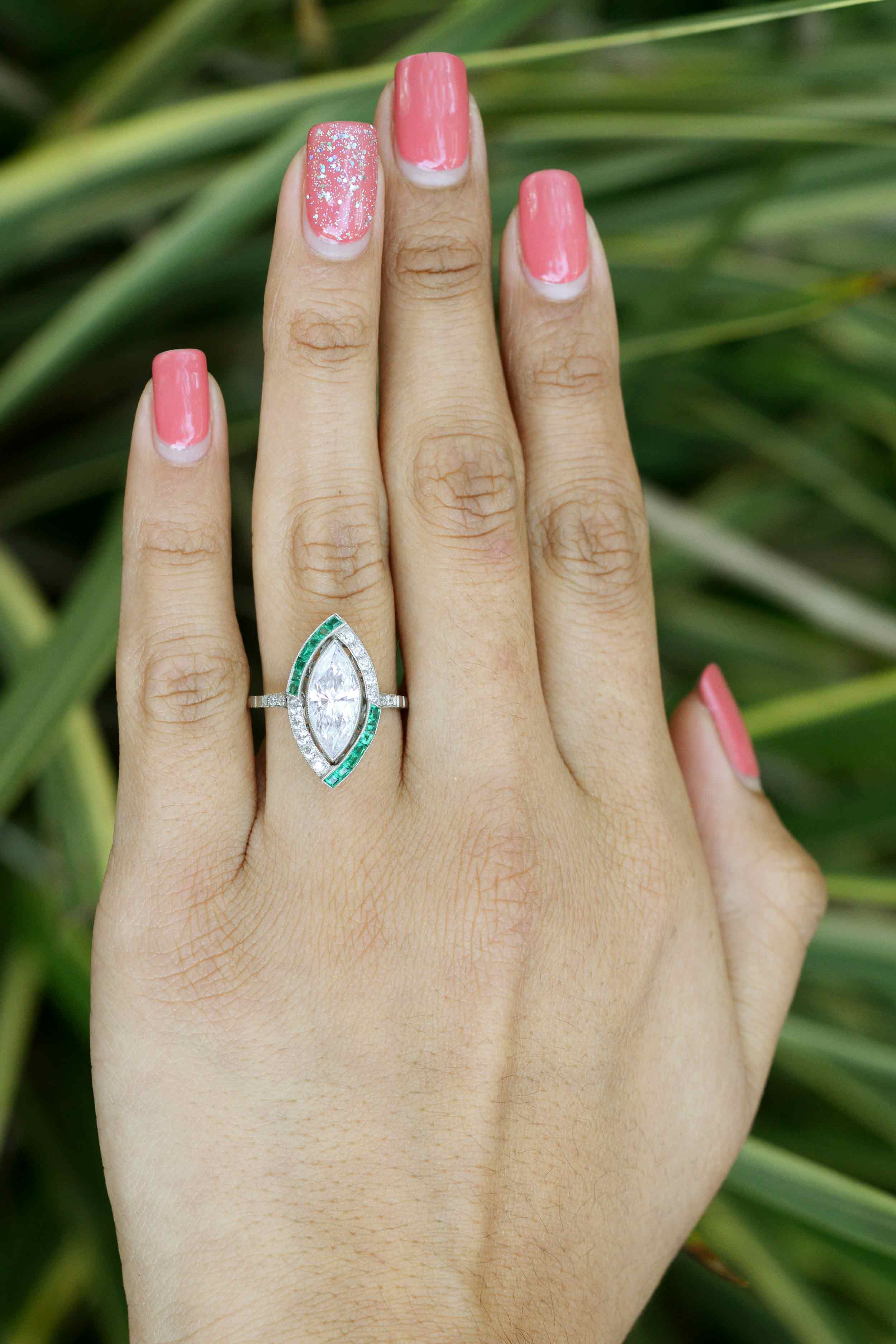 A unique marquise diamond and emerald engagement ring with a split halo pattern.