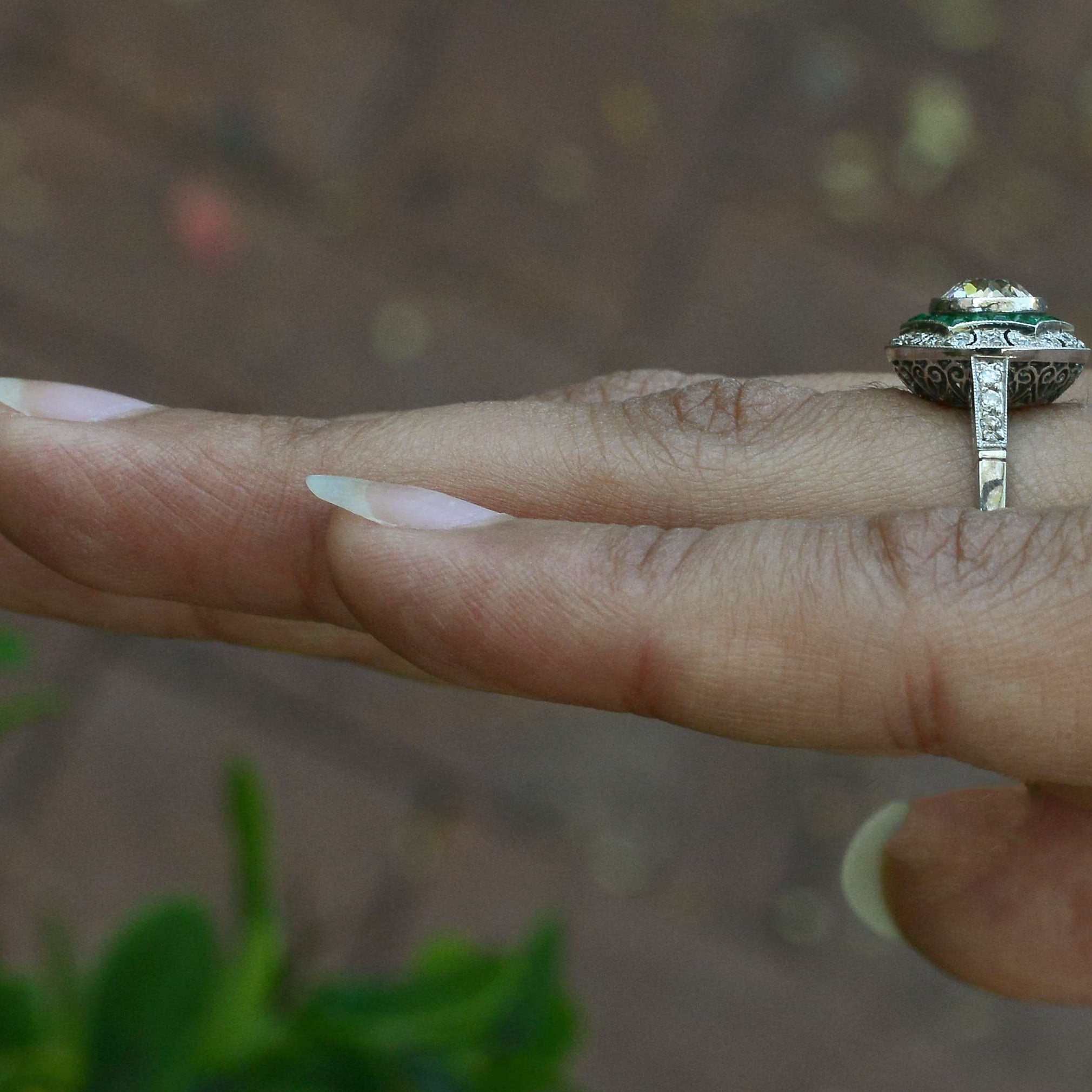 A large diamond art deco engagement ring surrounded by a halo of emeralds.
