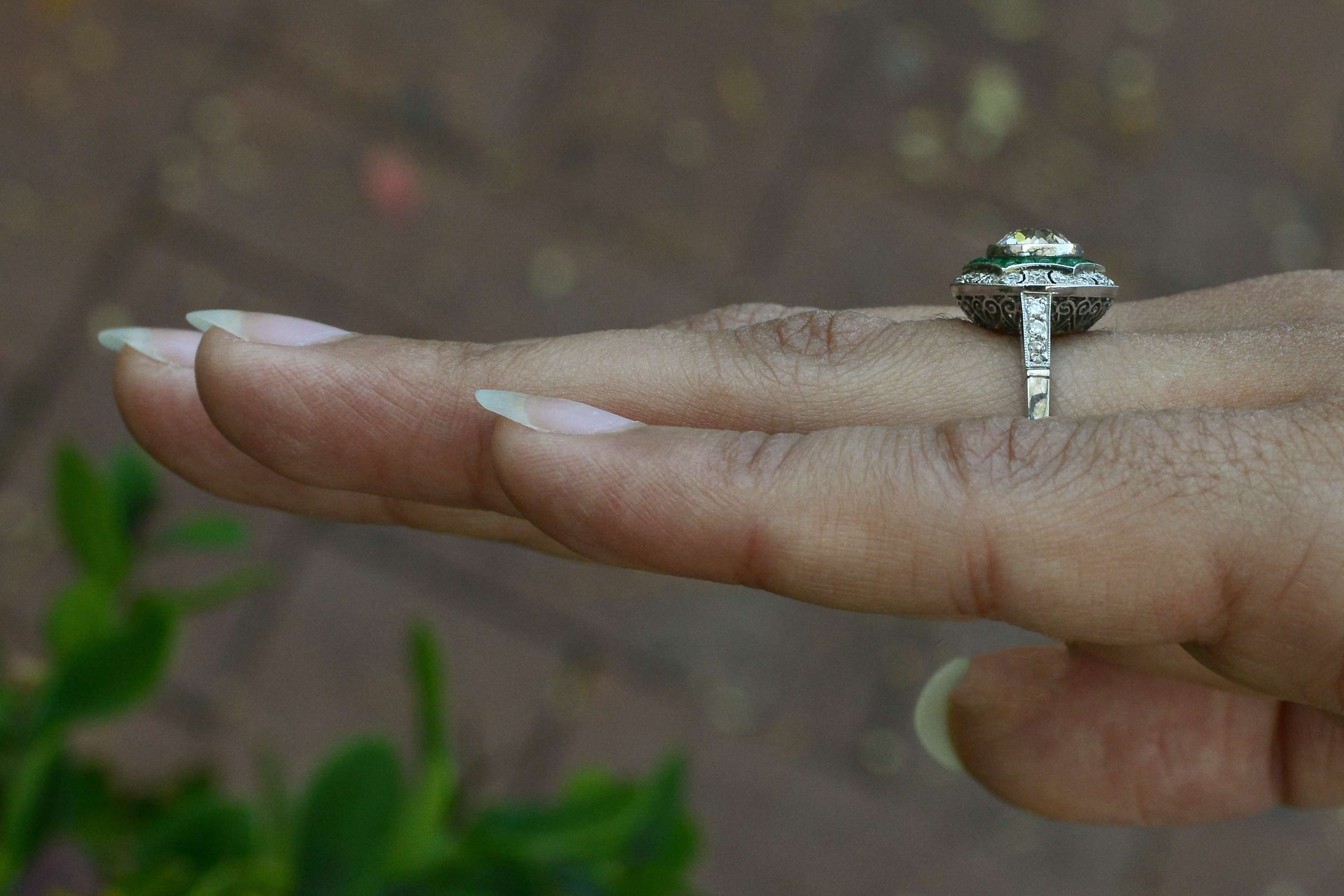 A large diamond art deco engagement ring surrounded by a halo of emeralds.