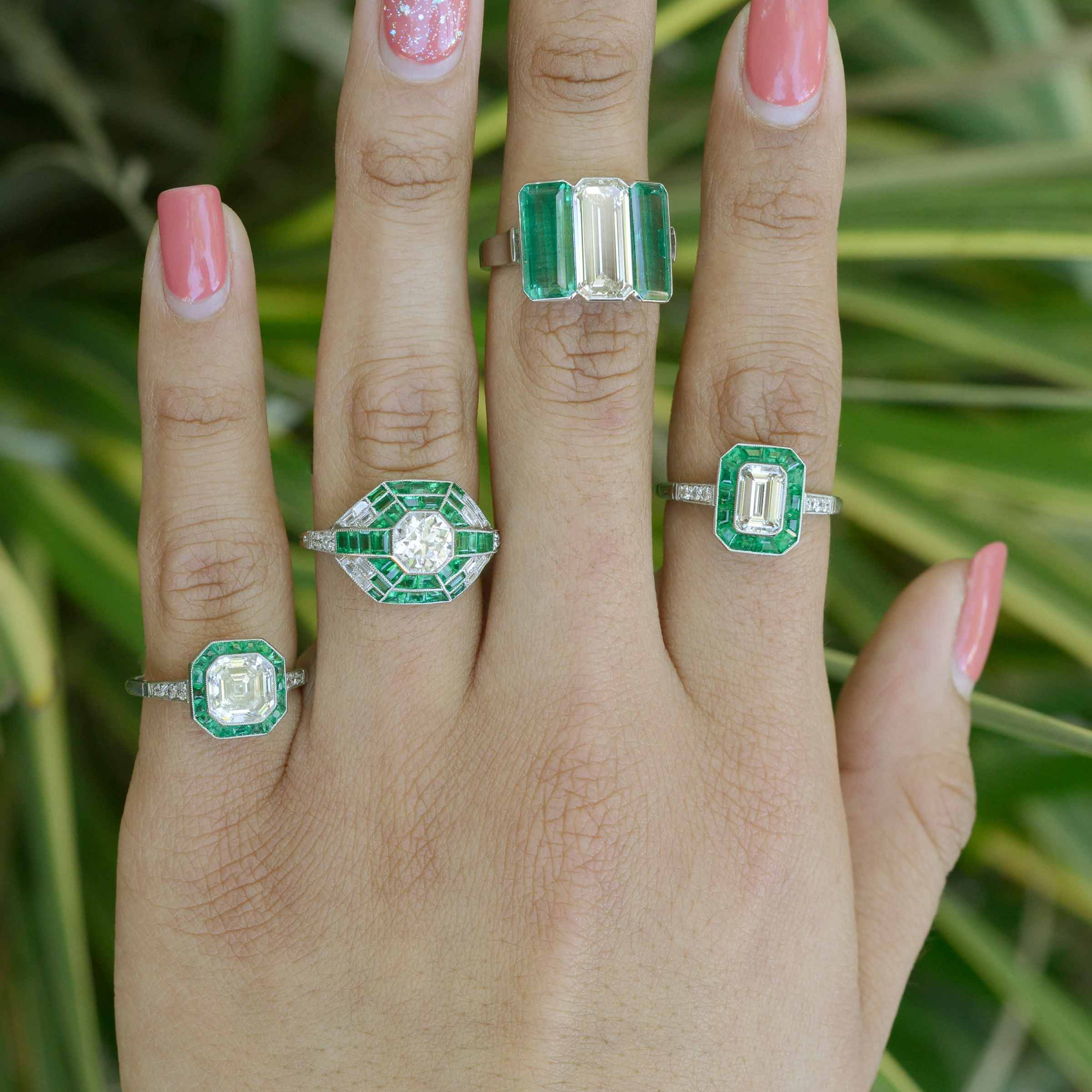 These engagement rings feature a large diamond and several emerald accent gemstones.