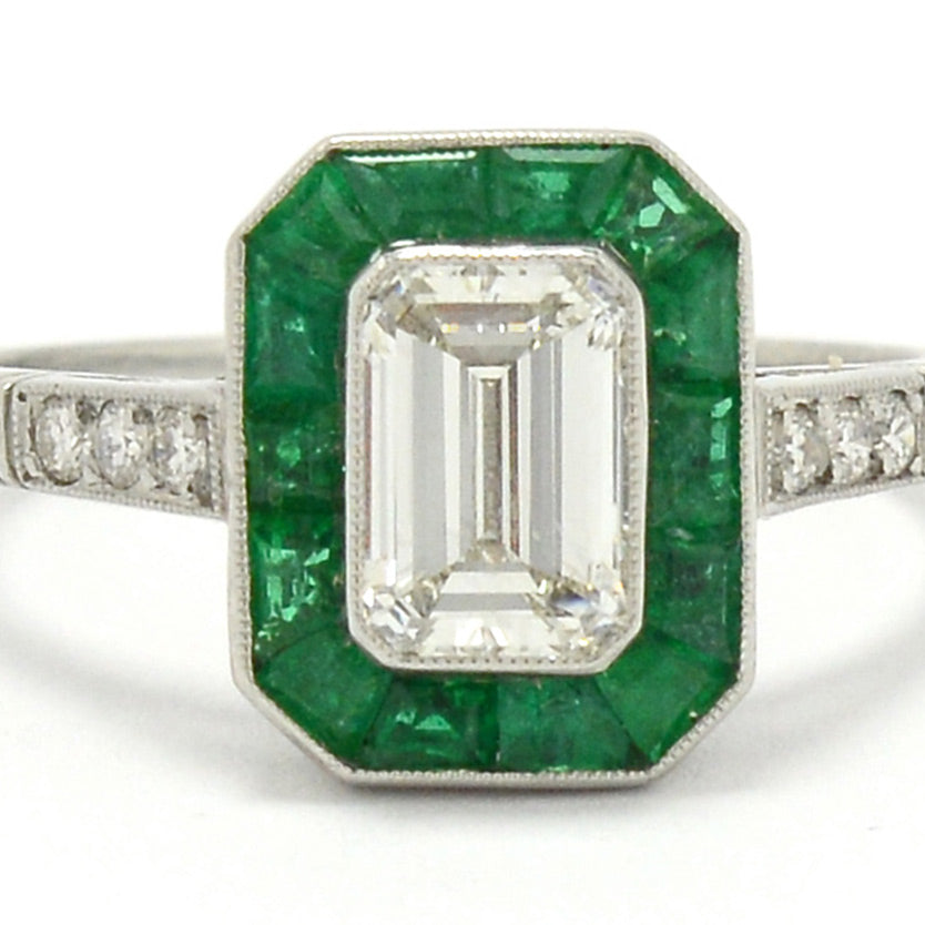 An h color and vs2 clarity 1 carat emerald cut diamond engagement ring with a halo of emeralds.