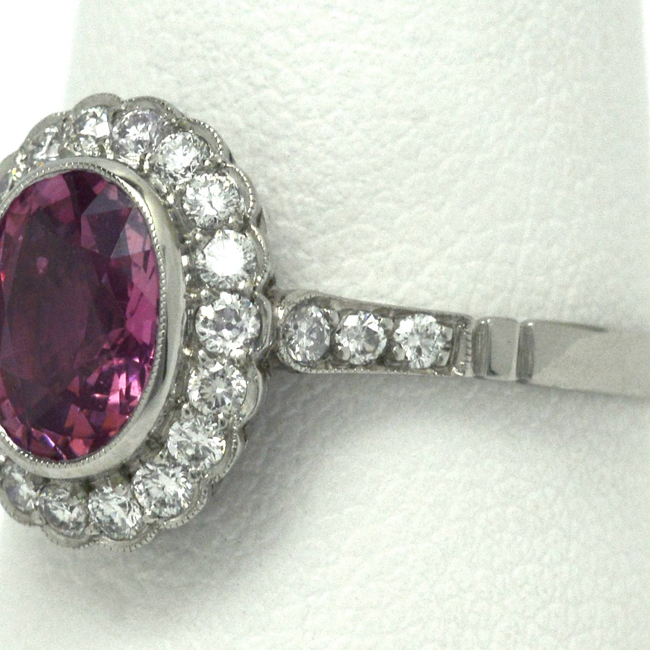 A milgrain diamond halo engagement ring, set with a natural, oval pink sapphire.
