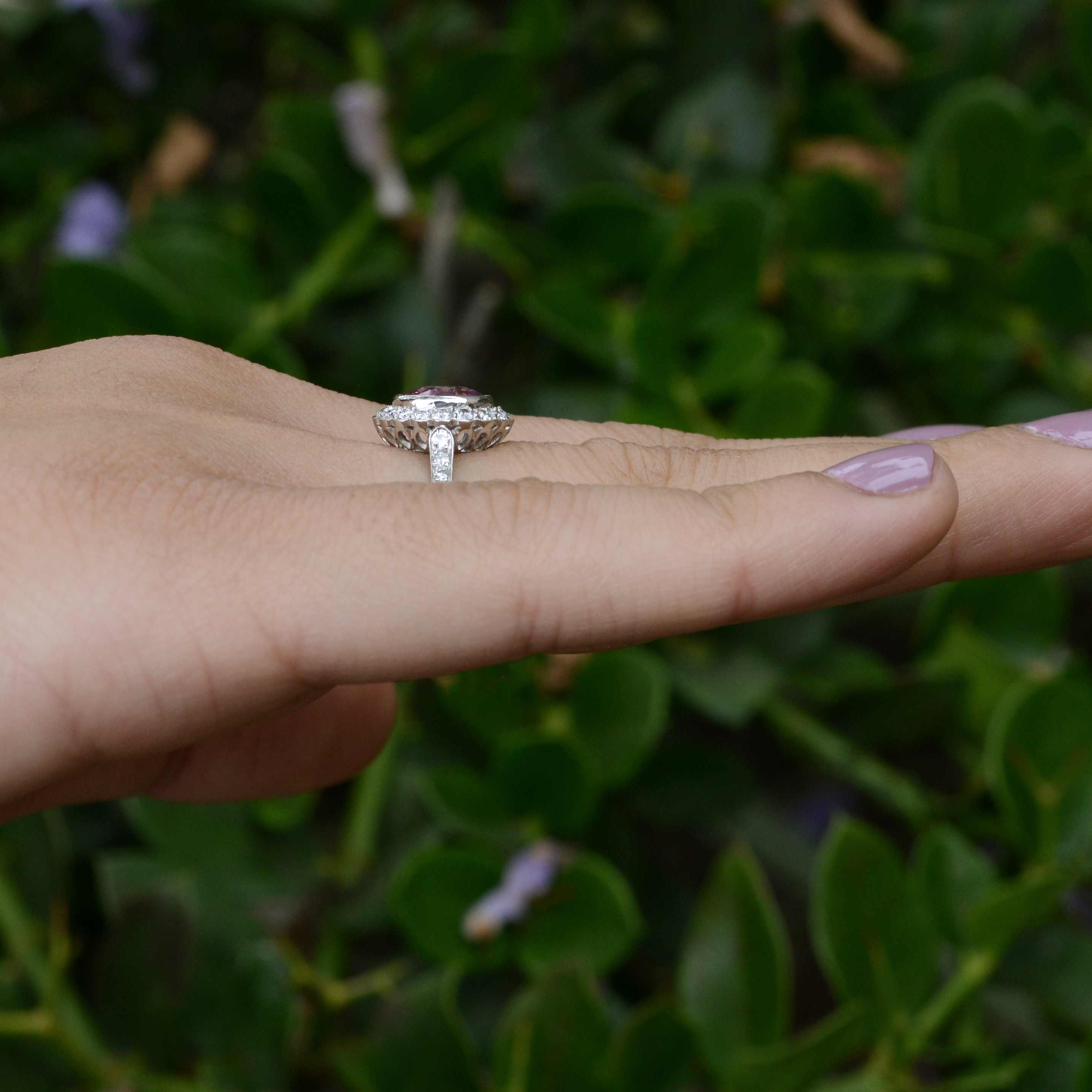 An oval pink sapphire set in a scalloped diamond halo engagement ring.