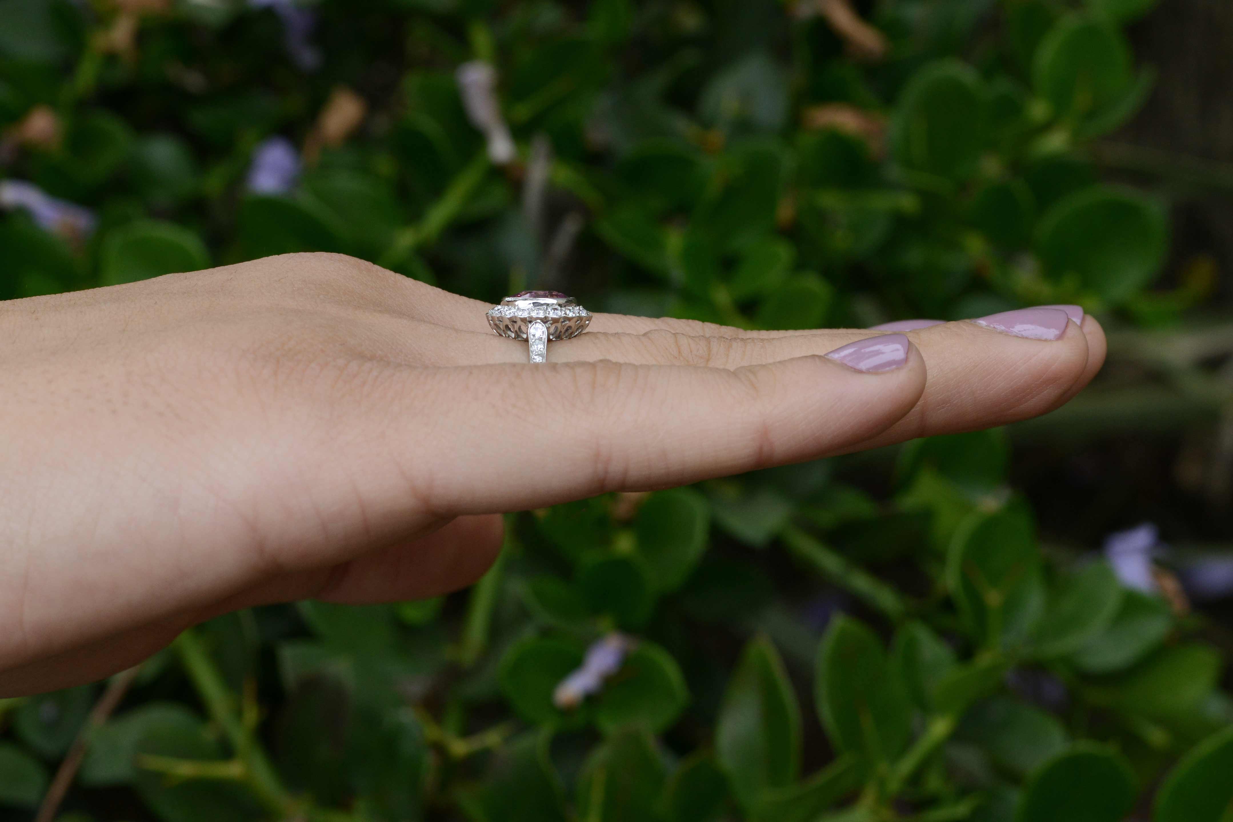 An oval pink sapphire set in a scalloped diamond halo engagement ring.