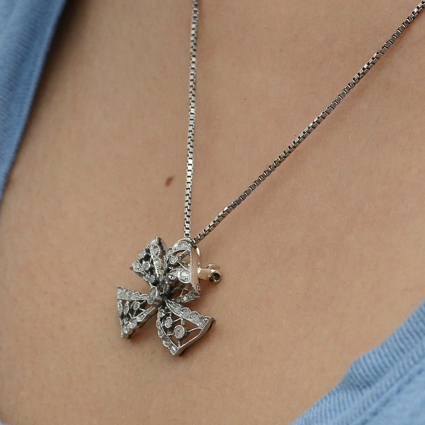 A white gold chain holds an antique platinum diamond bow pendant.