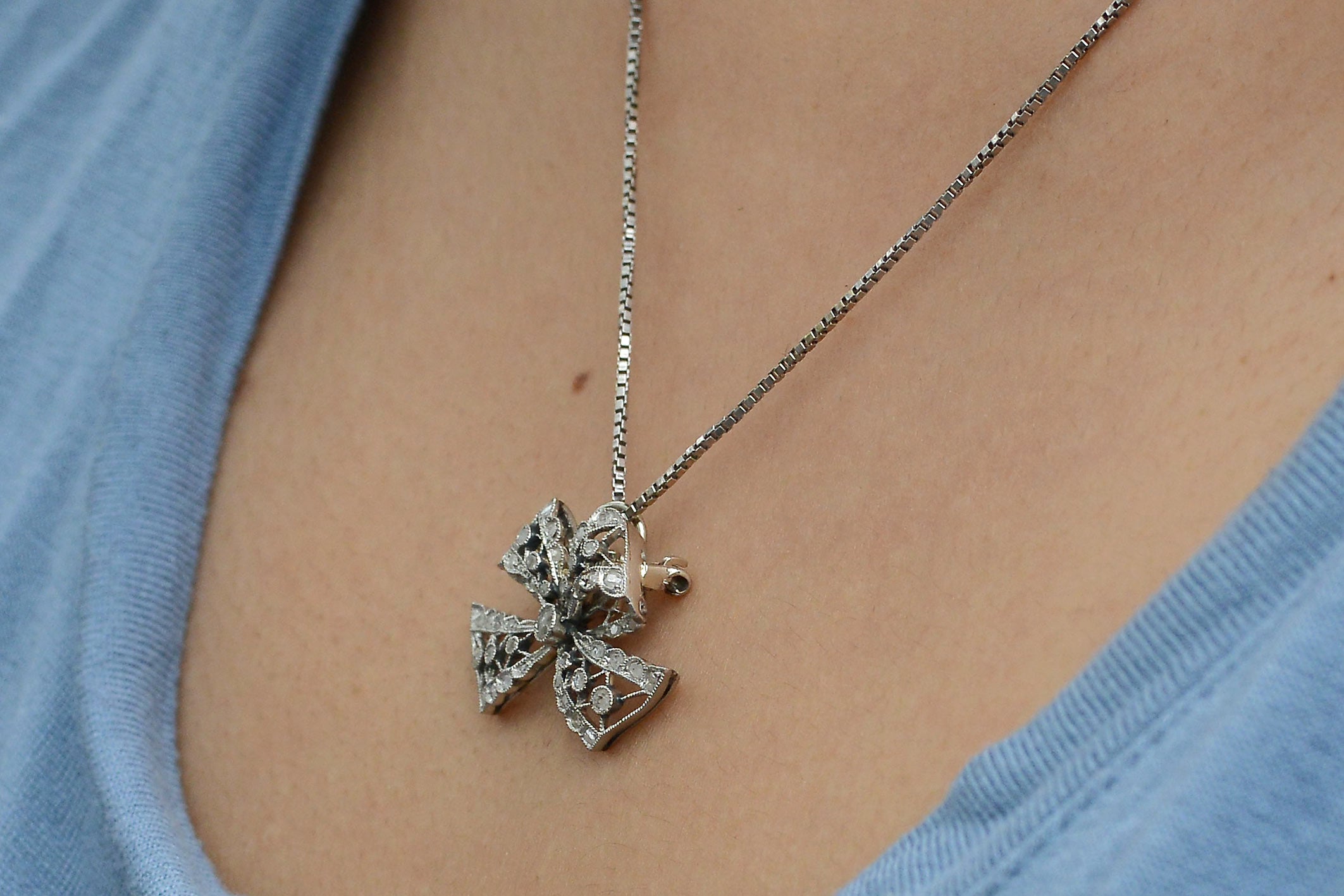A white gold chain holds an antique platinum diamond bow pendant.