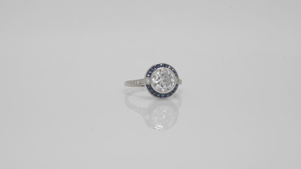 A sparkling round brilliant diamond of over a carat set in a platinum target setting with sapphires.