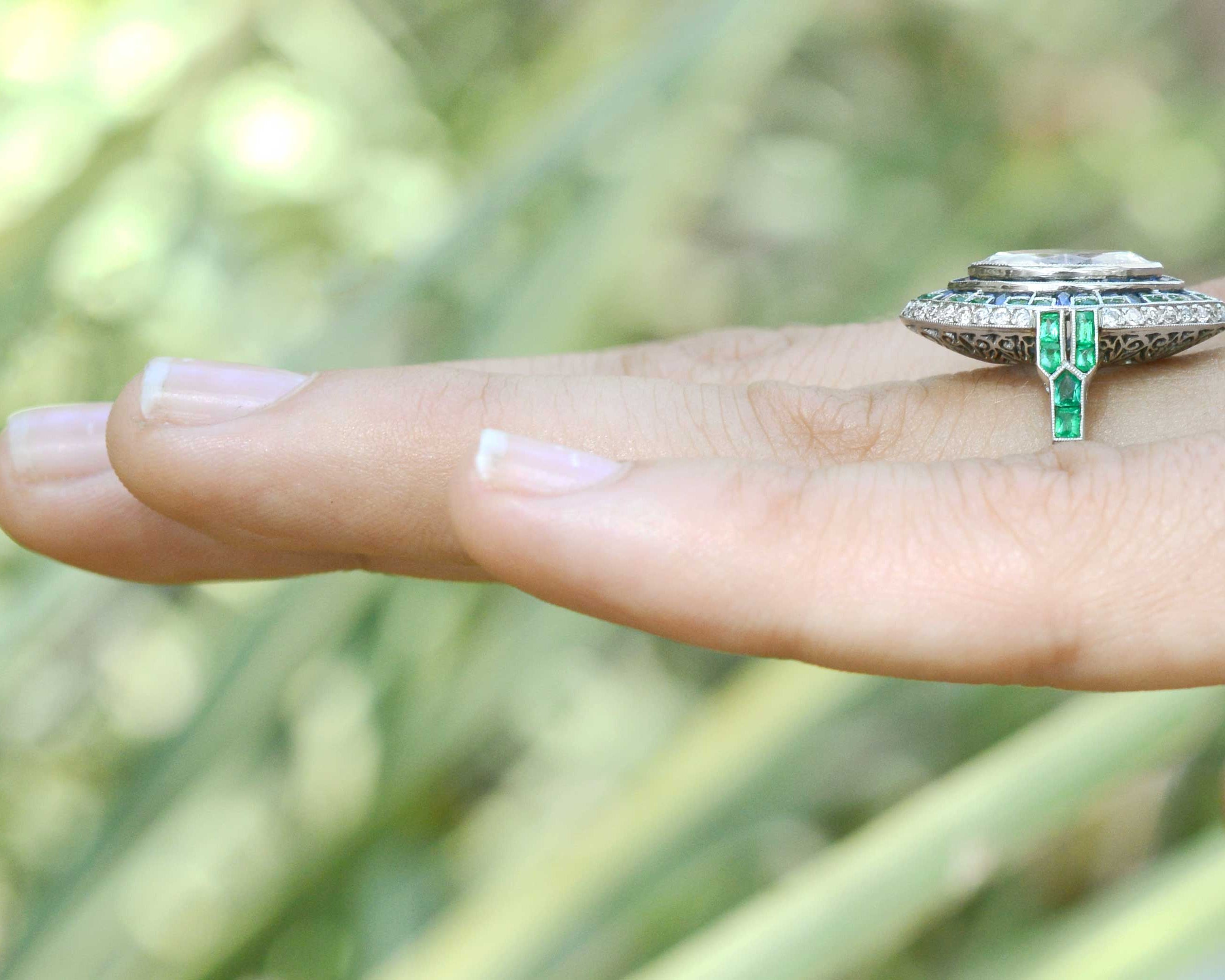 A platinum marquise diamond wedding ring with a halo of sapphires and emeralds.