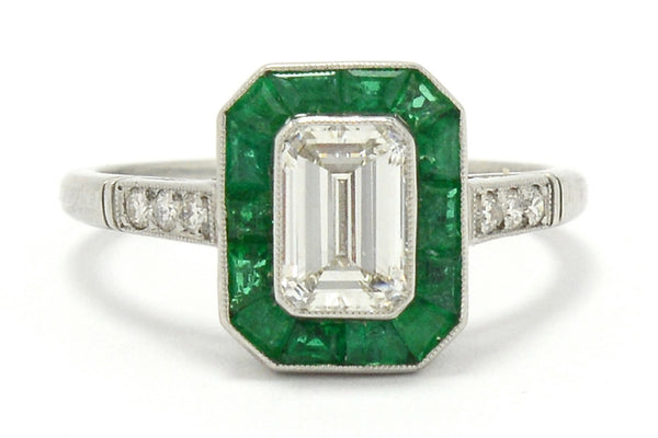 An h color and vs2 clarity 1 carat emerald cut diamond engagement ring with a halo of emeralds.